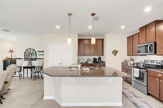 kitchen featuring a kitchen island with sink, light tile patterned flooring, hanging light fixtures, and appliances with stainless steel finishes