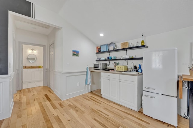 kitchen with lofted ceiling, white refrigerator, white cabinets, and light wood-type flooring