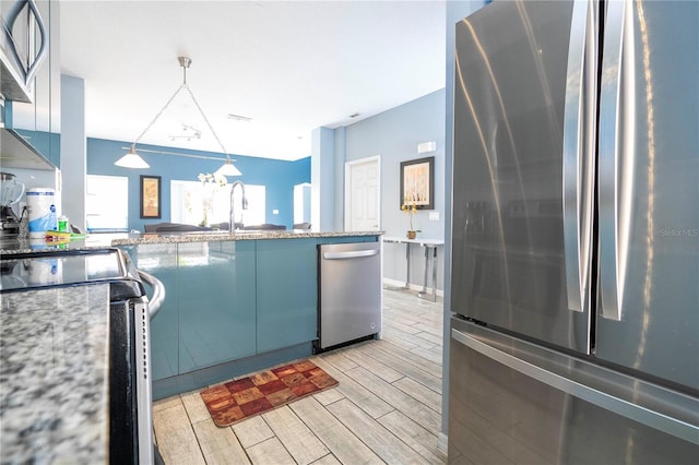 kitchen featuring stainless steel appliances, decorative light fixtures, light wood-type flooring, sink, and light stone counters