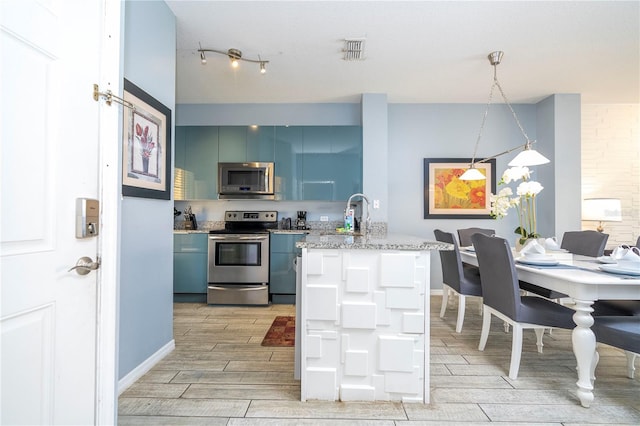 kitchen featuring appliances with stainless steel finishes, rail lighting, decorative light fixtures, light wood-type flooring, and blue cabinetry