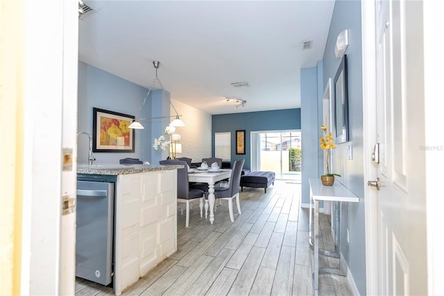 kitchen with white cabinetry, stainless steel dishwasher, hanging light fixtures, and light wood-type flooring