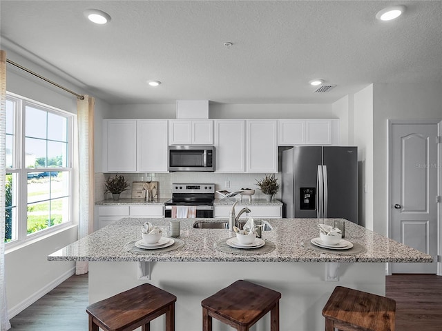 kitchen with a kitchen bar, appliances with stainless steel finishes, tasteful backsplash, a kitchen island with sink, and white cabinets