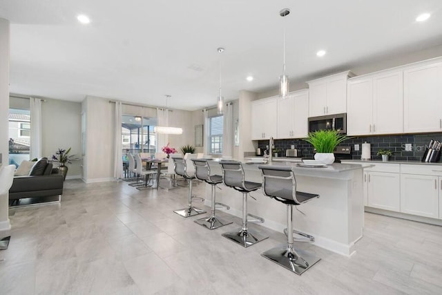 kitchen with white cabinetry, a breakfast bar area, backsplash, hanging light fixtures, and a center island with sink