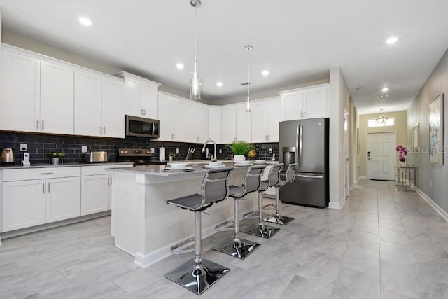 kitchen with appliances with stainless steel finishes, white cabinets, pendant lighting, backsplash, and an island with sink