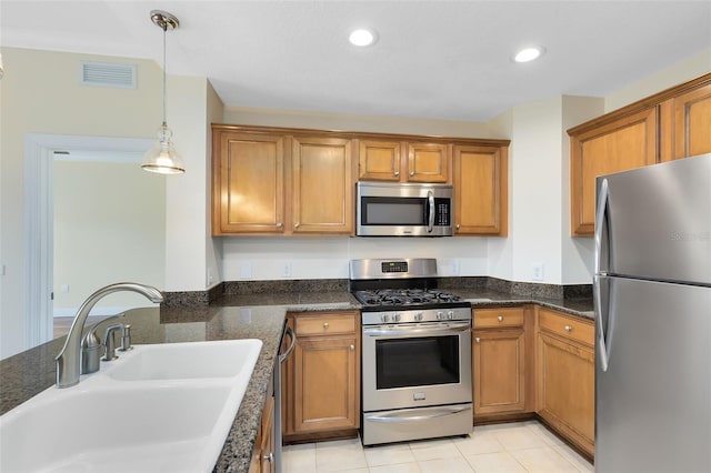 kitchen with pendant lighting, appliances with stainless steel finishes, dark stone countertops, sink, and light tile patterned floors