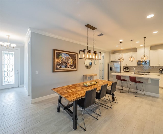 dining space with ornamental molding, sink, an inviting chandelier, and light wood-type flooring