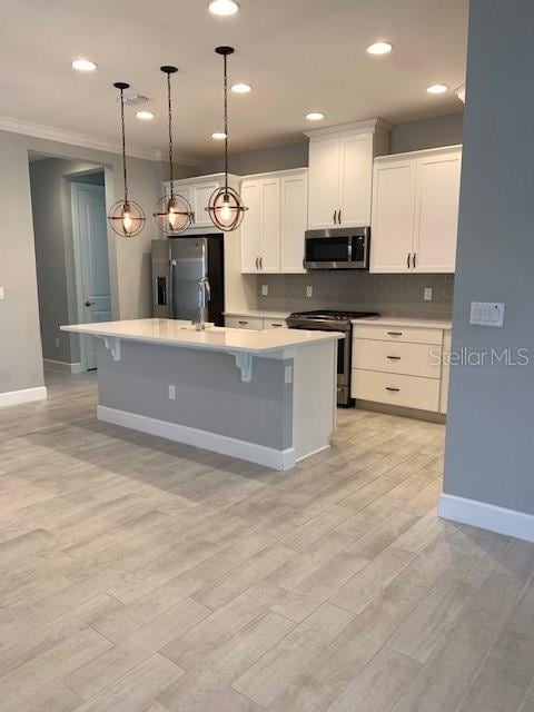 kitchen featuring decorative light fixtures, white cabinets, backsplash, stainless steel appliances, and a center island with sink