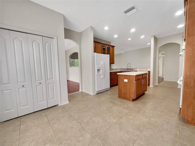 kitchen with light tile patterned flooring, sink, white fridge with ice dispenser, and a center island