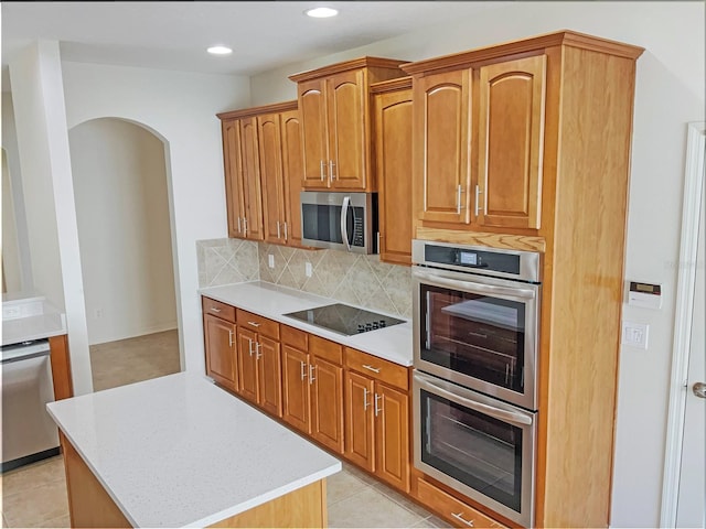 kitchen with appliances with stainless steel finishes, light stone counters, light tile patterned flooring, a center island, and tasteful backsplash