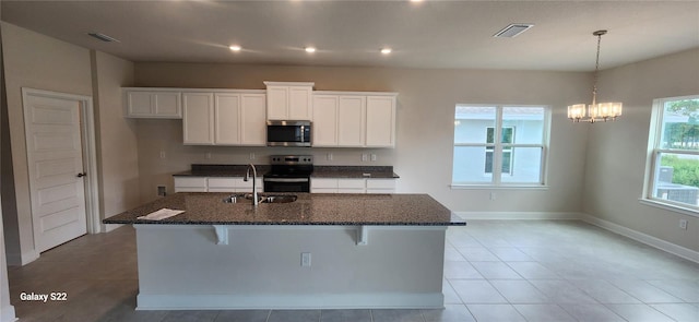 kitchen with a kitchen bar, a center island with sink, dark stone countertops, appliances with stainless steel finishes, and white cabinets