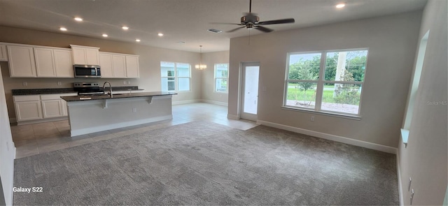 kitchen with plenty of natural light, light carpet, stove, and an island with sink