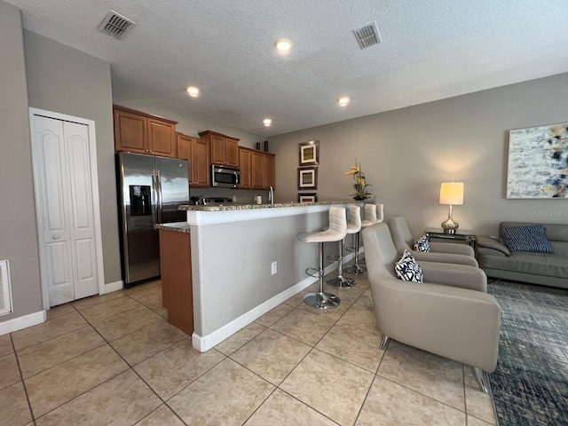 kitchen with appliances with stainless steel finishes, a breakfast bar, light tile patterned floors, a center island with sink, and a textured ceiling