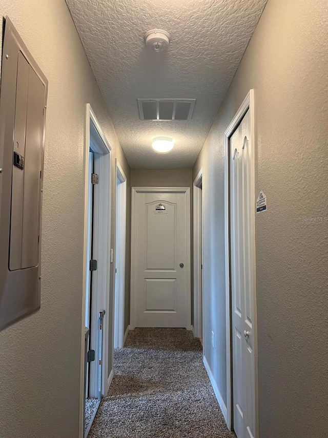 hall with electric panel, a textured ceiling, and dark colored carpet