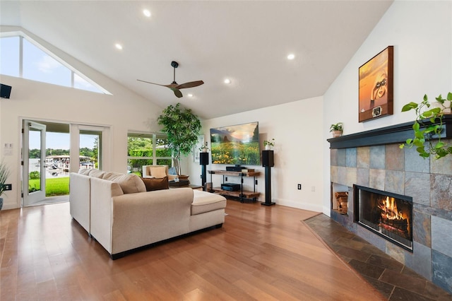 living room featuring ceiling fan, high vaulted ceiling, a tiled fireplace, and hardwood / wood-style floors