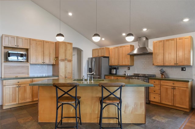 kitchen featuring decorative light fixtures, a center island with sink, wall chimney exhaust hood, and appliances with stainless steel finishes