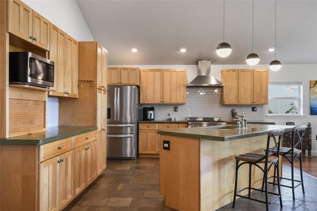 kitchen with wall chimney exhaust hood, tasteful backsplash, decorative light fixtures, appliances with stainless steel finishes, and an island with sink