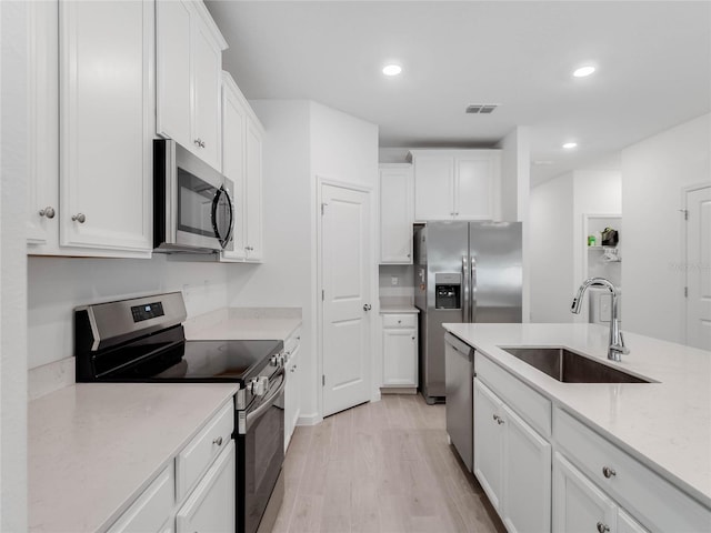 kitchen featuring sink, light stone counters, light hardwood / wood-style flooring, appliances with stainless steel finishes, and white cabinets