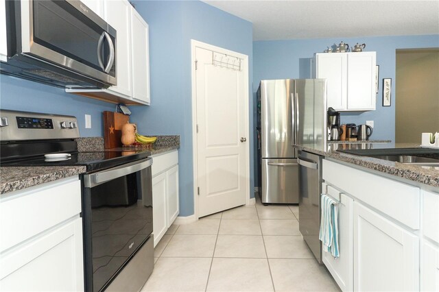 kitchen featuring appliances with stainless steel finishes, dark stone counters, light tile patterned floors, and white cabinetry