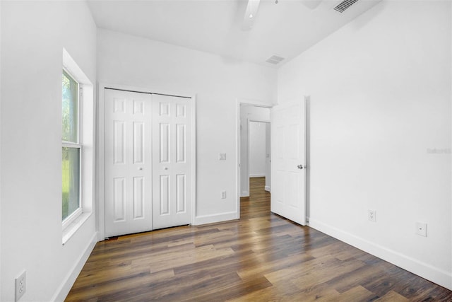 unfurnished bedroom featuring multiple windows, dark hardwood / wood-style flooring, a closet, and ceiling fan