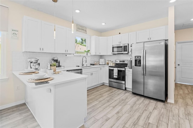 kitchen featuring light hardwood / wood-style flooring, stainless steel appliances, white cabinets, sink, and hanging light fixtures