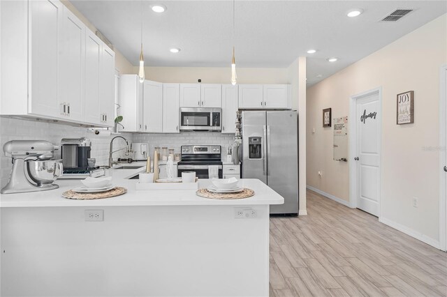 kitchen featuring white cabinets, pendant lighting, appliances with stainless steel finishes, and light wood-type flooring