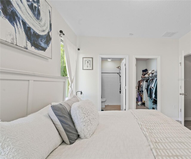 bedroom featuring a walk in closet, connected bathroom, and hardwood / wood-style floors