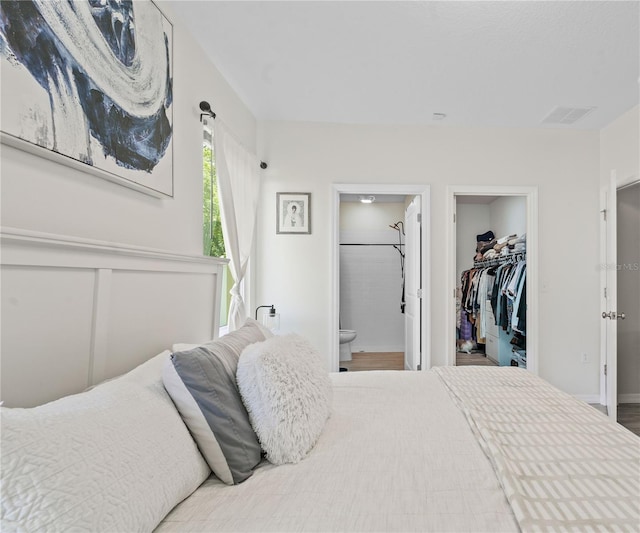 bedroom with connected bathroom, hardwood / wood-style flooring, and a walk in closet