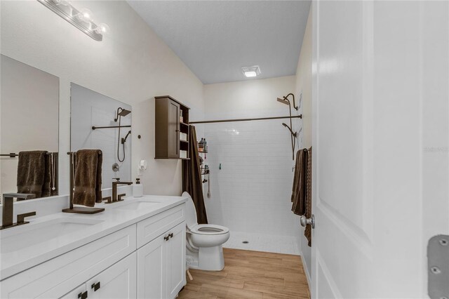 bathroom with toilet, dual vanity, hardwood / wood-style floors, and a tile shower