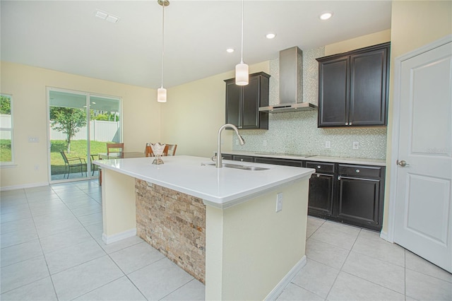 kitchen featuring an island with sink, sink, backsplash, hanging light fixtures, and wall chimney exhaust hood