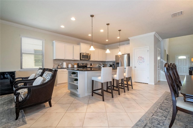 kitchen featuring appliances with stainless steel finishes, white cabinets, backsplash, light tile patterned floors, and a kitchen island with sink