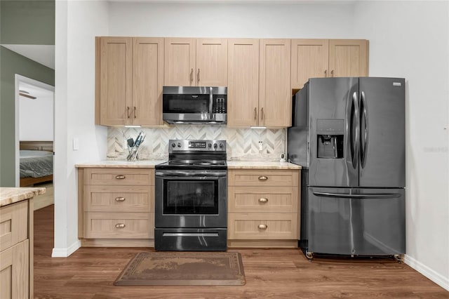 kitchen with hardwood / wood-style flooring, backsplash, light brown cabinets, and stainless steel appliances