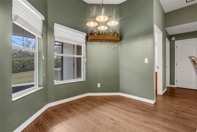 unfurnished dining area featuring hardwood / wood-style flooring, a healthy amount of sunlight, and an inviting chandelier