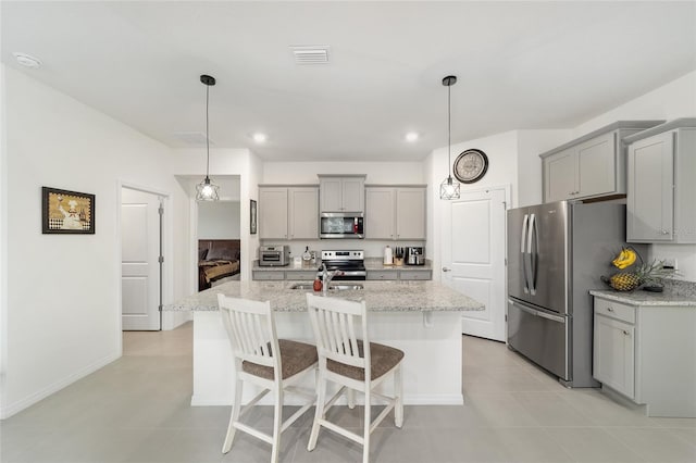 kitchen with stainless steel appliances, hanging light fixtures, light tile patterned floors, a kitchen island with sink, and light stone countertops