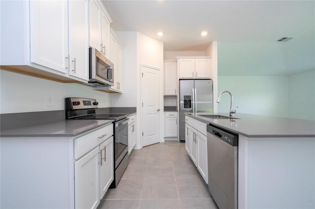 kitchen with sink, light tile patterned floors, appliances with stainless steel finishes, white cabinetry, and a center island with sink