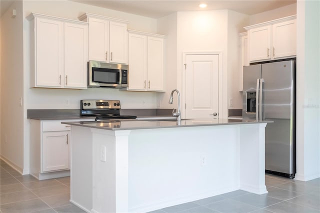 kitchen featuring stainless steel appliances, light tile patterned floors, a center island with sink, and white cabinets