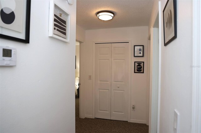 corridor featuring dark colored carpet and a textured ceiling