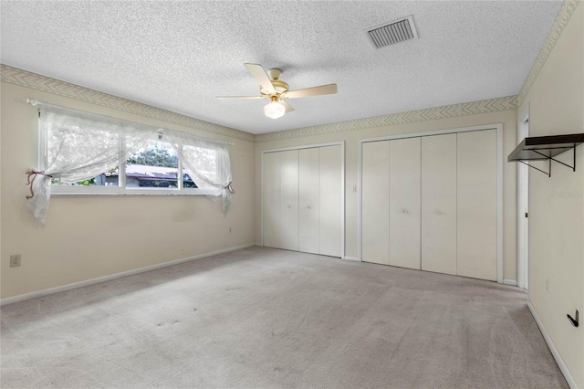 unfurnished bedroom featuring a textured ceiling, ceiling fan, light carpet, and two closets