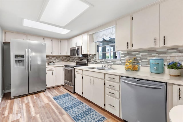 kitchen featuring light wood-type flooring, white cabinetry, backsplash, stainless steel appliances, and sink