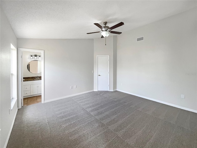 unfurnished bedroom featuring dark carpet, lofted ceiling, ensuite bath, ceiling fan, and a textured ceiling