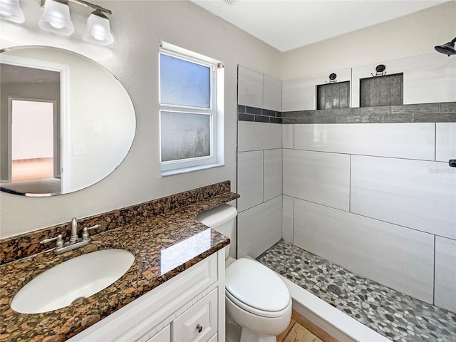 bathroom with a tile shower, vanity, and toilet