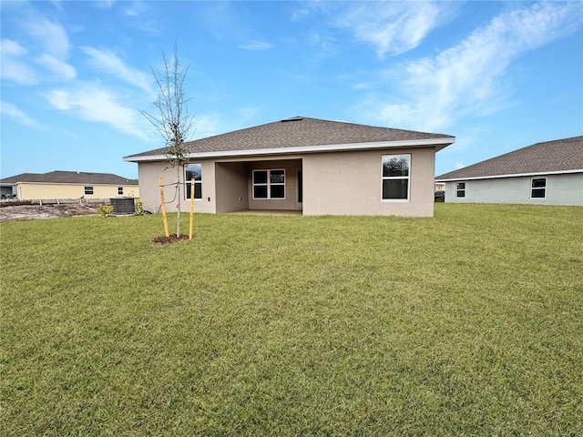 rear view of property with roof with shingles, a lawn, central AC unit, and stucco siding