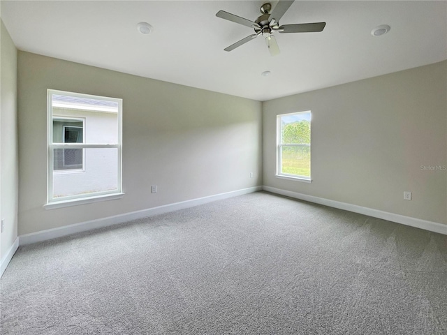 empty room featuring a ceiling fan, light colored carpet, and baseboards