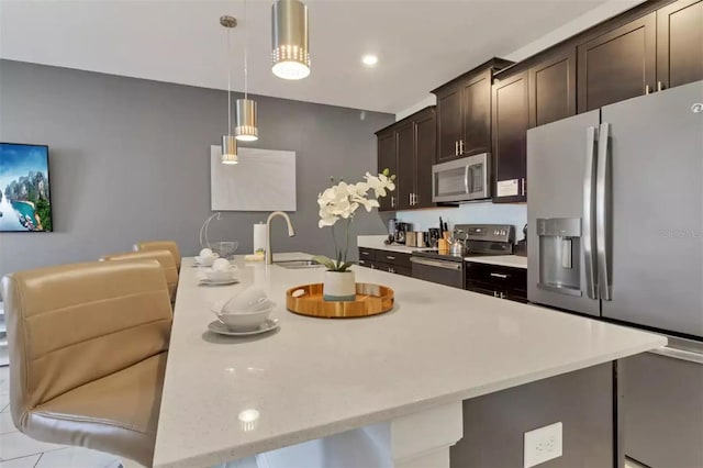 kitchen featuring dark brown cabinets, pendant lighting, sink, a breakfast bar area, and appliances with stainless steel finishes