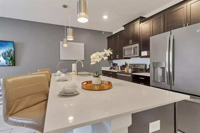 kitchen featuring pendant lighting, a sink, appliances with stainless steel finishes, a breakfast bar, and dark brown cabinetry