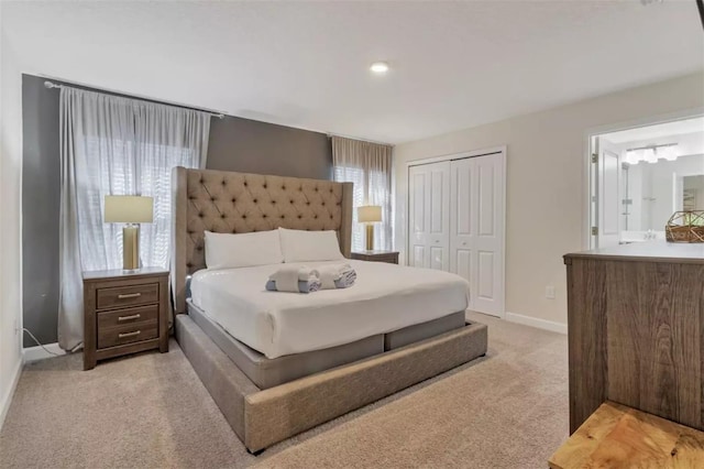 bedroom with ensuite bathroom, a closet, light colored carpet, and baseboards