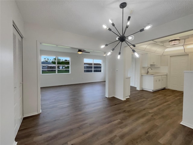 unfurnished living room featuring sink, ceiling fan with notable chandelier, a textured ceiling, and dark hardwood / wood-style flooring