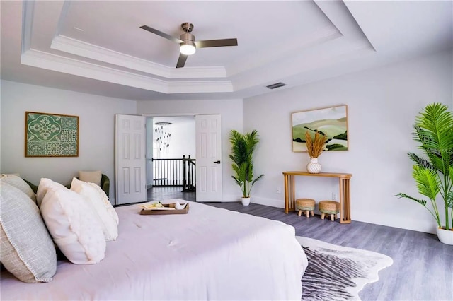 bedroom with ceiling fan, hardwood / wood-style floors, and a tray ceiling