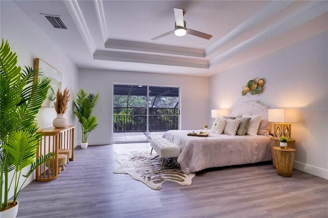 bedroom with hardwood / wood-style flooring, ceiling fan, access to outside, and a tray ceiling