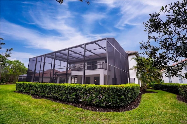 rear view of house with a balcony, a lawn, and a lanai