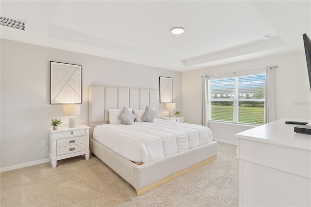 bedroom with light colored carpet and a tray ceiling